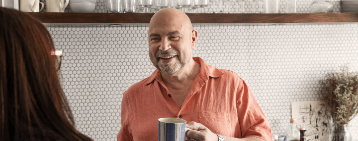 Middle-aged man smiling, holding coffee and talking with a woman